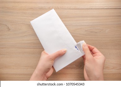 Woman's hand holds and opens a white paper envelope or letter envelopes on a wooden desk top view background.