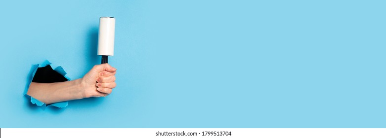 Woman's hand holds roller for cleaning clothes on a blue background. Banner.