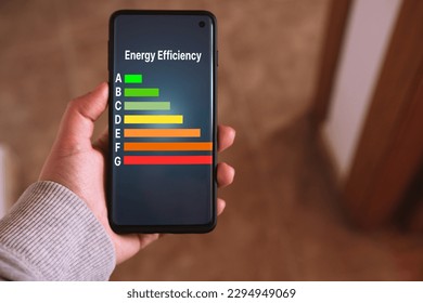 Woman's hand holds a smartphone with a Energy efficiency rating labels on screen. Low consumption and efficient products. Reduce carbon footprint. Green eco-friendly business. Low CO2 emissions. - Powered by Shutterstock