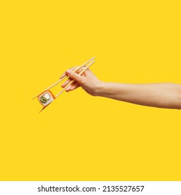 Woman's hand holds sticks sushi roll yellow background - Powered by Shutterstock