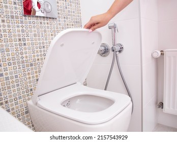 A woman's hand holds the toilet lid in the toilet. The concept of cleanliness and hygiene in the bathroom, pleasant smell of freshness - Shutterstock ID 2157543929