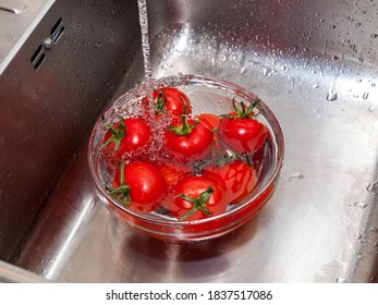 a woman's hand holds tomatoes under running tap water, the importance of handling and thoroughly washing vegetables and fruits during the covid-19 coronavirus pandemic - Powered by Shutterstock