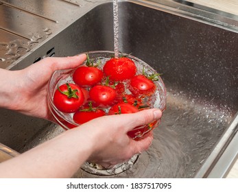 a woman's hand holds tomatoes under running tap water, the importance of handling and thoroughly washing vegetables and fruits during the covid-19 coronavirus pandemic - Powered by Shutterstock