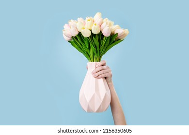 A woman's hand holds a vase with a bouquet of tulips on a blue background. - Powered by Shutterstock