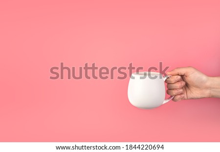 A woman's hand holds a white mug on a pink background. Background with space to copy, side view.
