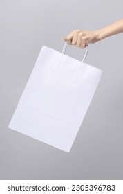 Woman's hand holds white paper shopping bag on gray background. Template for design, layout, mockup
