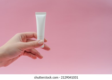 Woman's hand holds white plastic tubes on pink background. Сosmetic bottles for beauty or medicine products - Shutterstock ID 2129041031