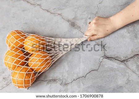 A woman's hand holds a white string bag with oranges on a dark background. Environmental care, waste recycling.