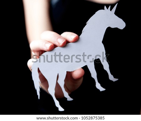 A woman's hand holds a white unicorn with a black background paper