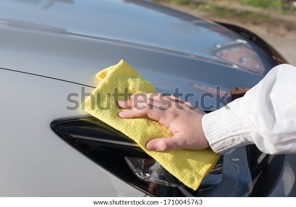 woman\'s hand  holds\
yellow cloth and washes white car, cleaning or polishing  vehicle,\
car maitenance