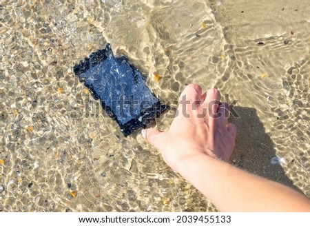 A woman's hand lifts a her smartphone from sea water on the beach. Lost and found accessories or property at vacation time, concept image.