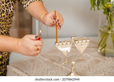 A Woman's Hand Lights Candles In A Hanukkah Lamp On The First Day Of Hanukkah On The Table Next To Fresh Donuts In A Plate.