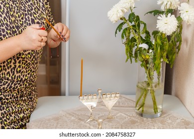 A Woman's Hand Lights Candles In A Hanukkah Lamp On The First Day Of Hanukkah On The Table Next To Fresh Donuts In A Plate.