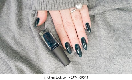 Woman's hand hand and long nails   black green manicure and bottles nail polish