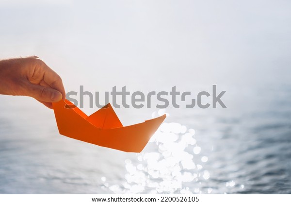 A woman\'s\
hand lowers a paper boat into the\
water