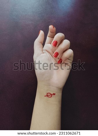 Woman's hand making arrow marks using henna on her wrist, isolated on maroon background.  Beautiful female hands with copy space.  The concept of reaching for something.