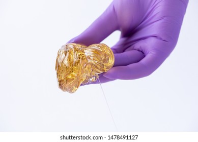 Woman's hand in a medical glove holds yellow sugar paste or wax for depilation close up on a white background