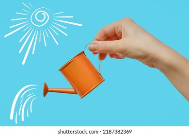 A woman's hand with a miniature orange watering can on a blue background. Close-up.