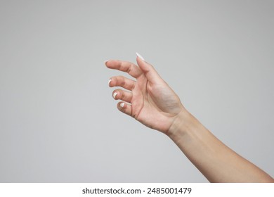 A woman's hand is open and holding something like a bottle. Gesture isolated on gray background. The girl gives some object. Product presentation concept or mockup with copy space. Advertising