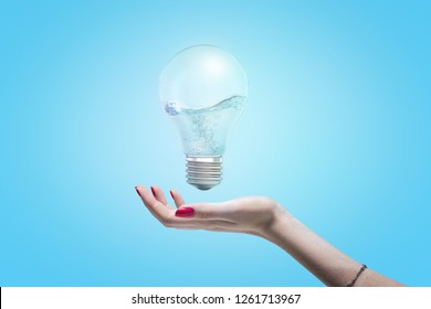 Woman's hand with open palm as if about to take hold of an electric bulb floating in the air with water inside the bulb. Generate new ideas. Creative thinking. Enlighten world.