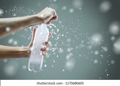 Женская рука открывает бутылку с газированной водой с брызгами и много капель на сером фоне. Студийная фотосъемка. Концепция здорового образа жизни