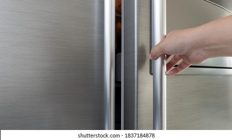 Woman's hand opening a gray metallic refrigerator door