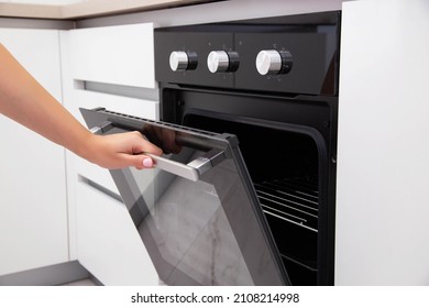 A woman's hand opens the door of an electric convection oven. Built-in oven in the kitchen - Shutterstock ID 2108214998