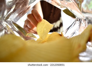 Woman's Hand Picking Up Yellow Potato Chips Inside A Bag Of Snacks.