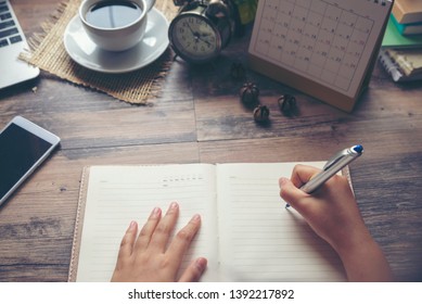 Woman's hand planner or organizer writing daily appointment, mark and noted schedule (meeting) on timetable or diary, work at home. Calendar, agenda, book, cup of coffee on desk. Planner concept.