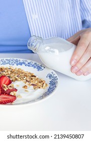 Woman's Hand Pouring Plant Based Milk Into Homemade Granola With Fresh Organic Strawberries And Yogurt In The Vintage Plate. Morning Breakfast Food Concept