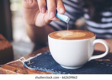 A Woman's Hand Pouring White Sugar In To White Hot Coffee Cup