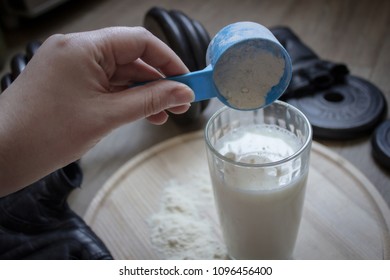 A Woman's Hand Pours The Protein Powder Into A Glass Of Milk. 