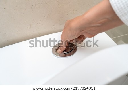 Woman's hand presses a button on a white toilet to flush