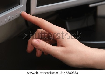 A woman's hand presses the power button on a computer monitor