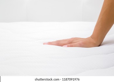 Woman's hand pressing on white mattress. Checking hardness and softness. Choice of the best type and quality. Side view. Close up.