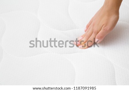 Woman's hand pressing on white mattress. Checking hardness and softness. Choice of the best type and quality. Close up.
