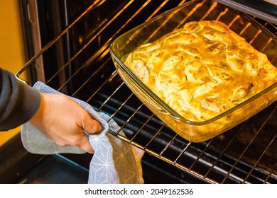 A Woman's Hand Pulls A Glass Container With A Traditional American Apple Pie From The Oven. Baking At Home. A Cooking Process Hot Food Dessert For Thanksgiving Day. Baking Pies At Fall Season.