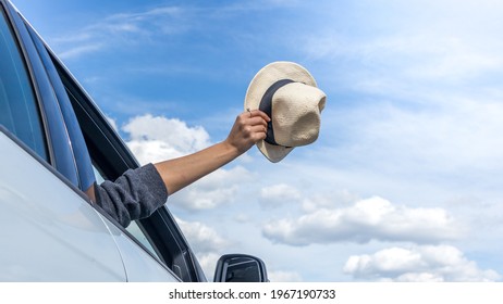 Woman's hand pulls a hat out of a car window. Freedom, travel and vacation concept.