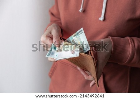 Woman's hand pulls various banknotes of Russian rubles out of worn leather wallet