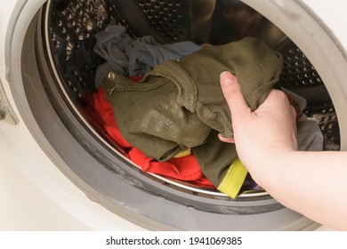 A Woman's Hand Puts Dirty Baby Clothes In The Washing Machine.Concept Washing Dirty Spots, The Best Means Of Cleaning Kids Clothes