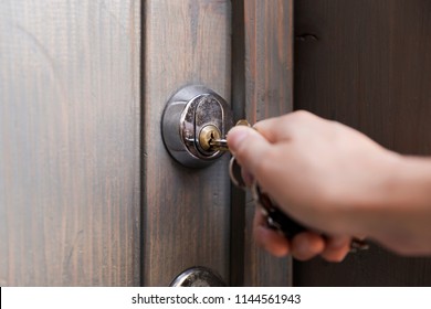Woman's hand puts the key in the keyhole of wooden door. Home security concept