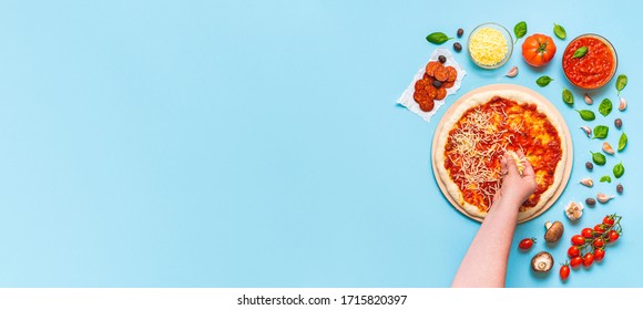 Woman's Hand Putting Cheese On Pizza. Top View With A Chef Making Pizza Step By Step. Pizza Ingredients On A Blue Table, Above View.