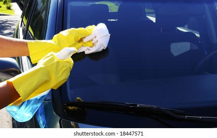 Woman's Hand With A Rag And Glass Cleaner Washing Windshield Glass Of An SUV Car