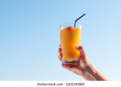 Woman's Hand Raising Glass With Refreshing Orange Cocktail In The Sky.