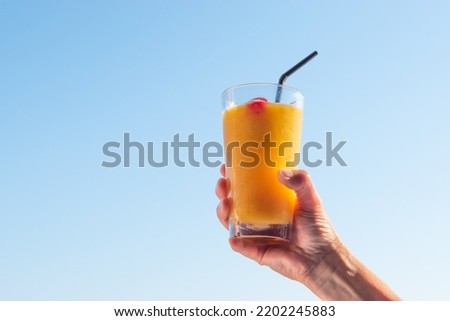 Woman's hand raising glass with refreshing orange cocktail in the sky.