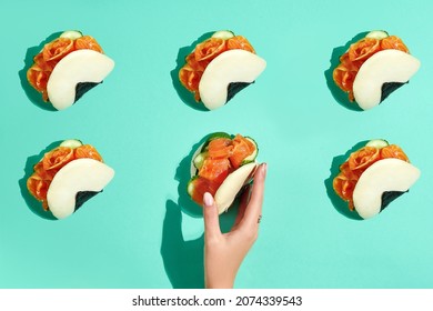 A woman's hand reaches for a bao bun with salmon. Bao buns pattern on turquoise background