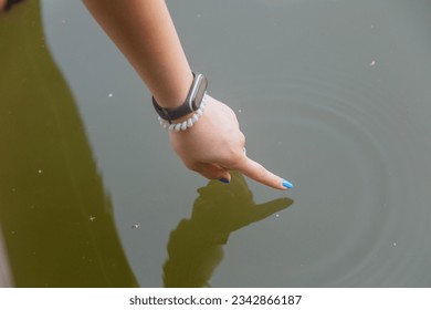 A woman's hand reaches out and touches a natural body of water, a freshwater lake. - Powered by Shutterstock