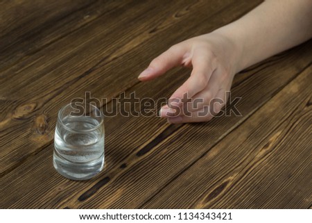 A woman's hand reaches for a wine-glass with alcohol, a wooden background, a close-up, a ghastly alcoholism