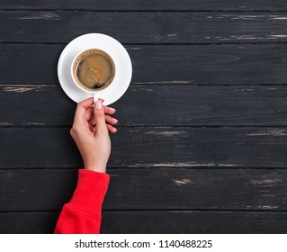 Woman's Hand In Red Clothing Holding A Cup Of Coffee On The Black Wooden Background, Top View