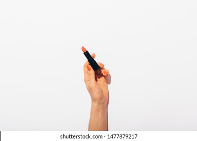 Woman's hand with red manicure holding lipstick casting hard shadow from the bright lighting on white background, top view.